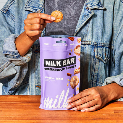 Front view of a bag of cinnamon toast crunchies,  with a human holding up a single cookie above the bag