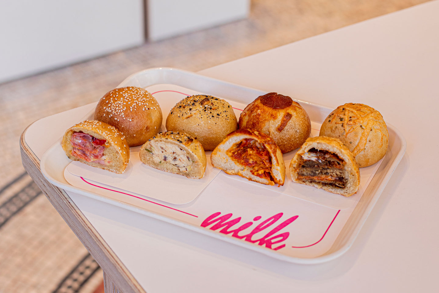 A side shot of a tray of savory baked breads on a table, featuring flavors like the Smokey Bacon Scallion Cream Cheese Bagel bomb and the Pepperoni Bagel Bomb.